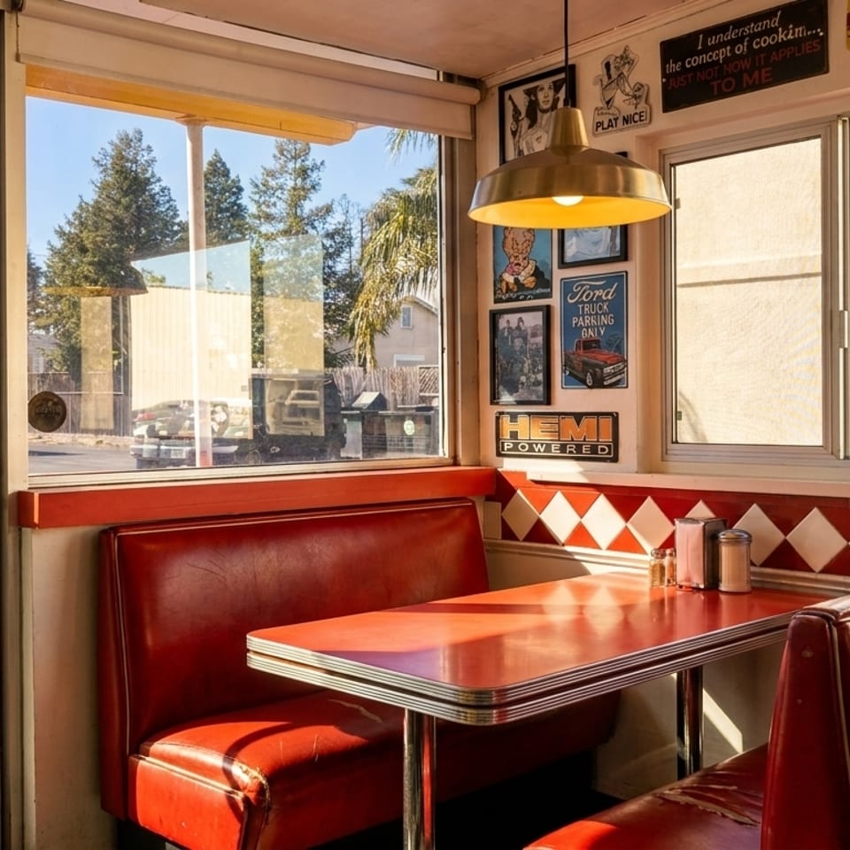 A retro diner booth with red seating, a red table, and vintage signs on the wall.