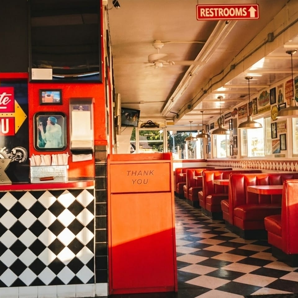Retro diner interior with red booths, checkerboard floor, and vintage Sno-White sign.